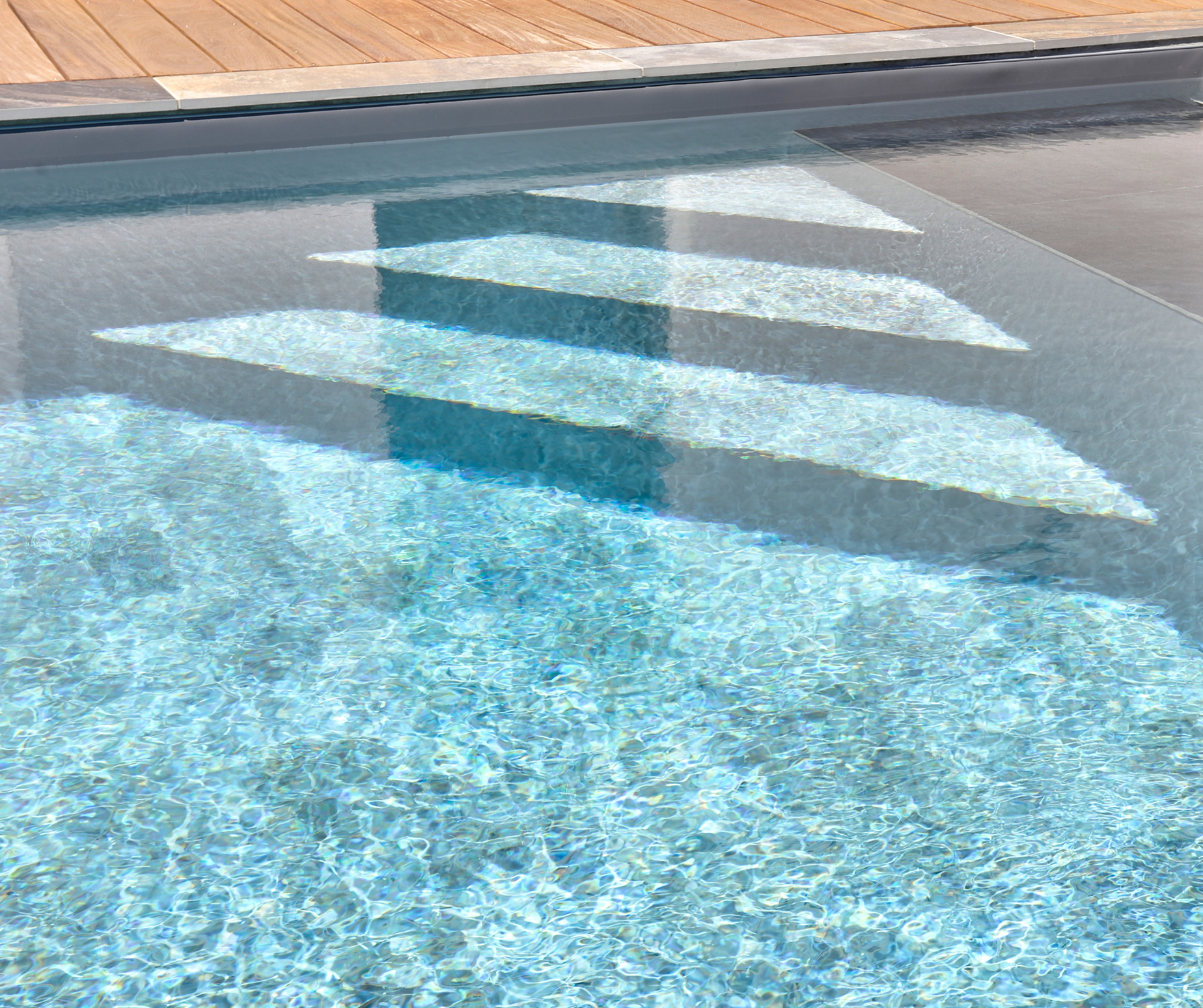 Escalier immergé d’une piscine moderne à eau cristalline avec plage en bois