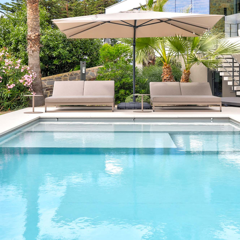 Piscine rectangulaire avec terrasse, bains de soleil et parasol dans un jardin