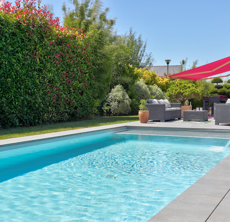 Piscine creusée extérieure rectangulaire avec terrasse en dalles grises et salon de jardin