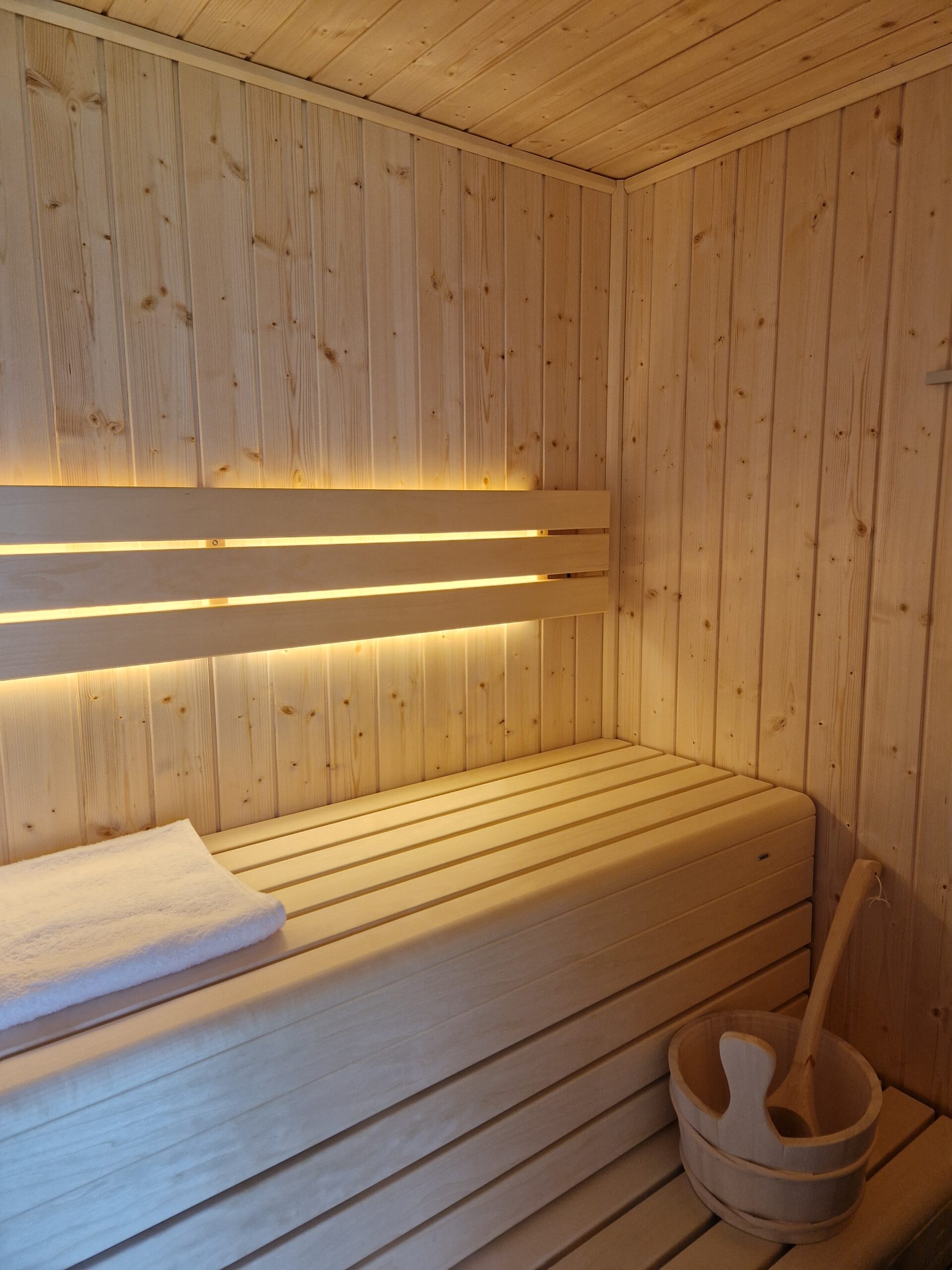 Intérieur de sauna en bois clair à Saint-Pever avec éclairage LED et seau