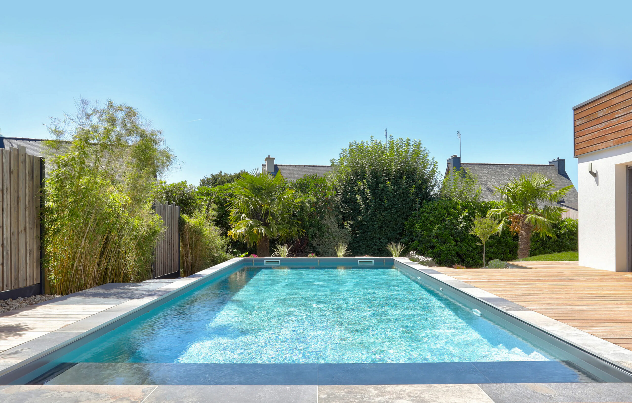 Piscine rectangulaire avec terrasse en bois et jardin paysager en Bretagne